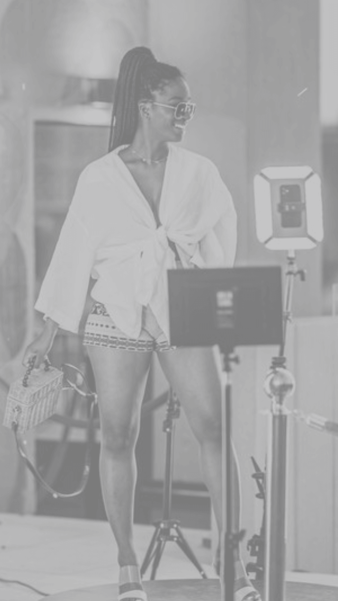 A black and white image of a woman standing next to a large 360 video booth platform with a camera mounted on top, designed for capturing video footage of guests at an event.